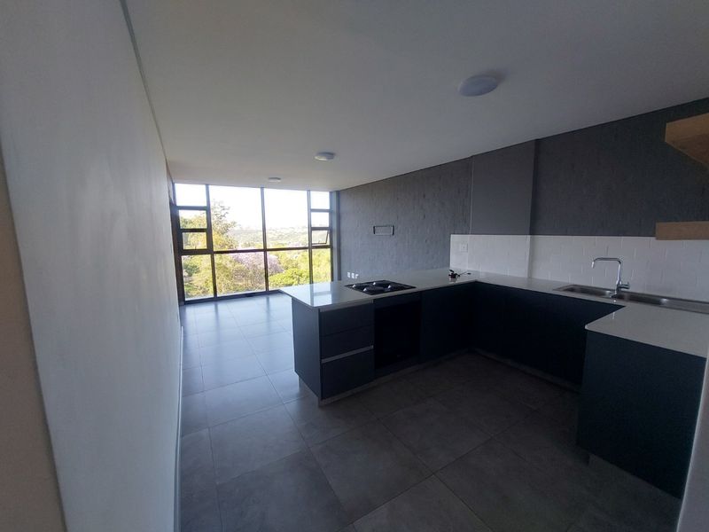 Modern open-plan kitchen and living area featuring sleek dark cabinetry, stone countertops, integrated hob, and expansive windows with natural light and scenic views.