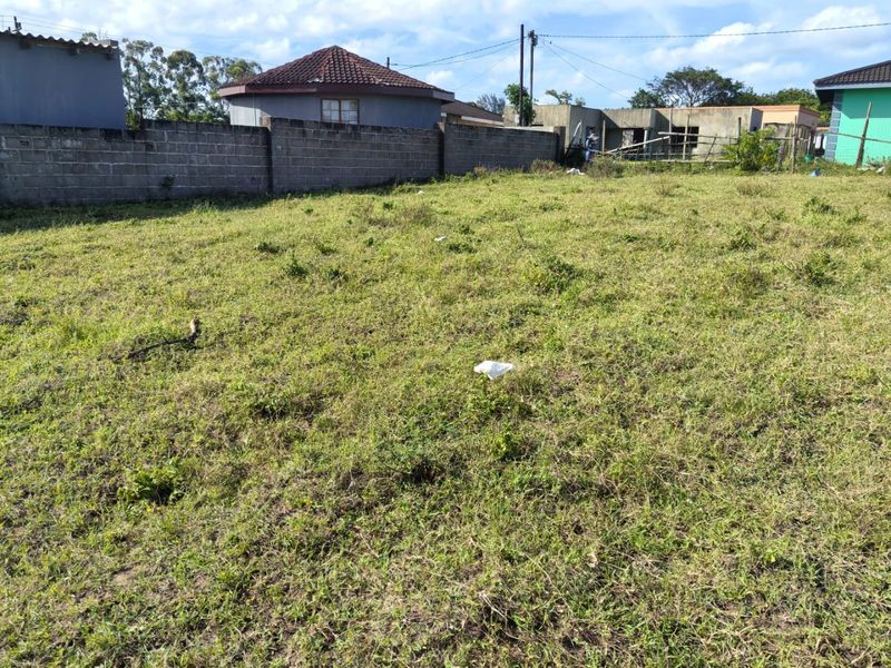 A vacant residential plot featuring a grassed area enclosed by a perimeter wall, suitable for future development.