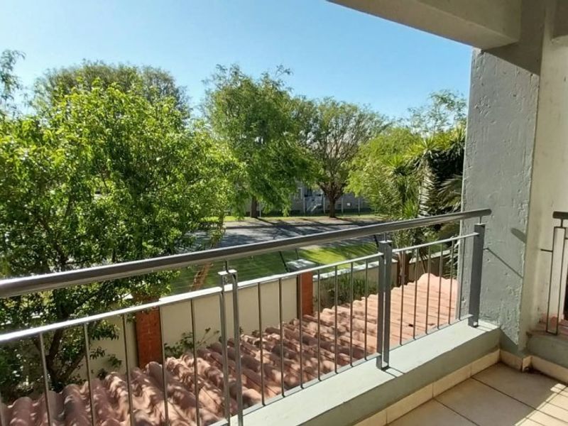 A covered balcony featuring a metal balustrade, tiled flooring, and views over the surrounding greenery and street.