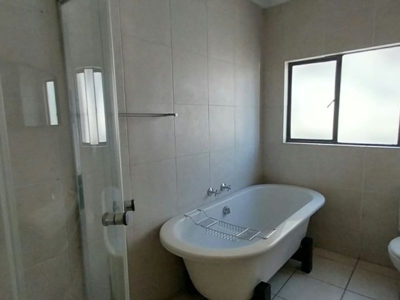 A clean, modern bathroom featuring a freestanding bathtub, a separate glass-enclosed shower, and neutral wall and floor tiling.