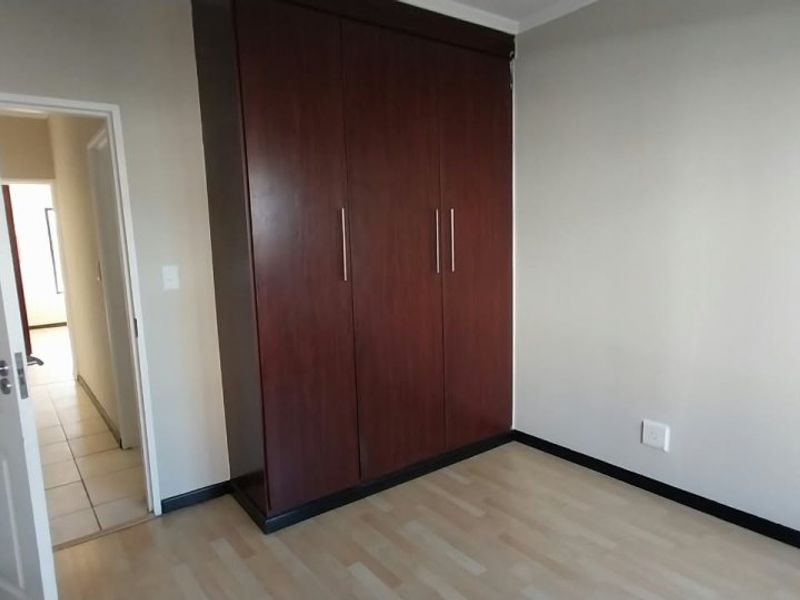 A clean, empty bedroom featuring light laminate flooring and a large, dark wood built-in wardrobe with modern handles.