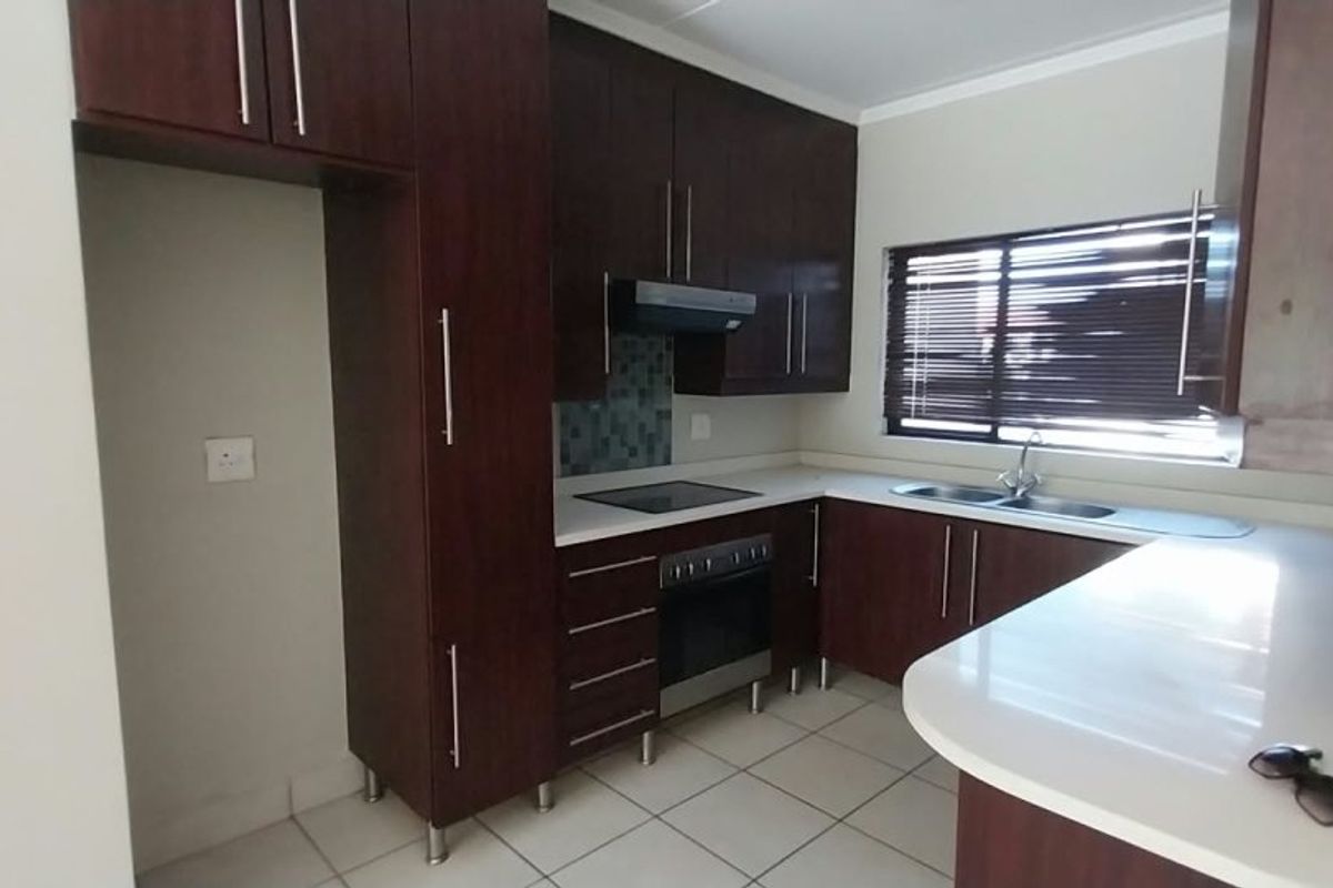 A functional kitchen featuring dark wood cabinetry, stone countertops, built-in oven, electric hob, and a double sink with tiled flooring.