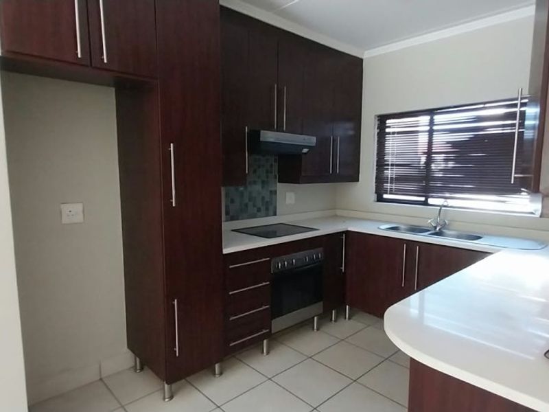 A functional kitchen featuring dark wood cabinetry, stone countertops, built-in oven, electric hob, and a double sink with tiled flooring.
