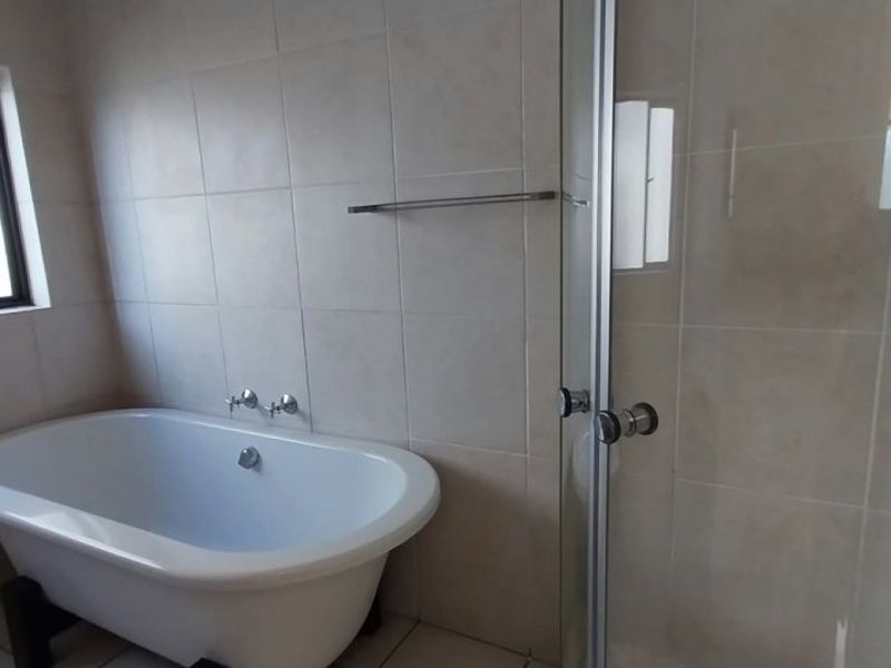 A clean, neutral-toned bathroom featuring a freestanding bathtub, a separate glass-enclosed shower, and tiled finishes throughout.
