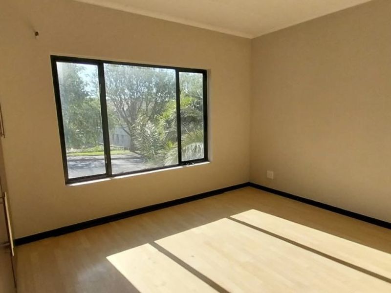 A bright, empty bedroom featuring laminate flooring, built-in cupboards, and large aluminium-framed windows allowing for ample natural light.