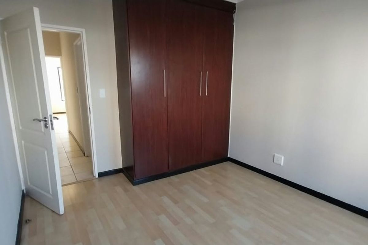 A clean, empty bedroom featuring light laminate flooring, neutral walls, and a large dark wood built-in wardrobe.