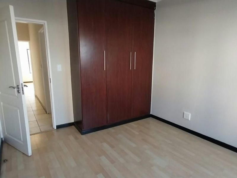 A clean, empty bedroom featuring light laminate flooring, neutral walls, and a large dark wood built-in wardrobe.