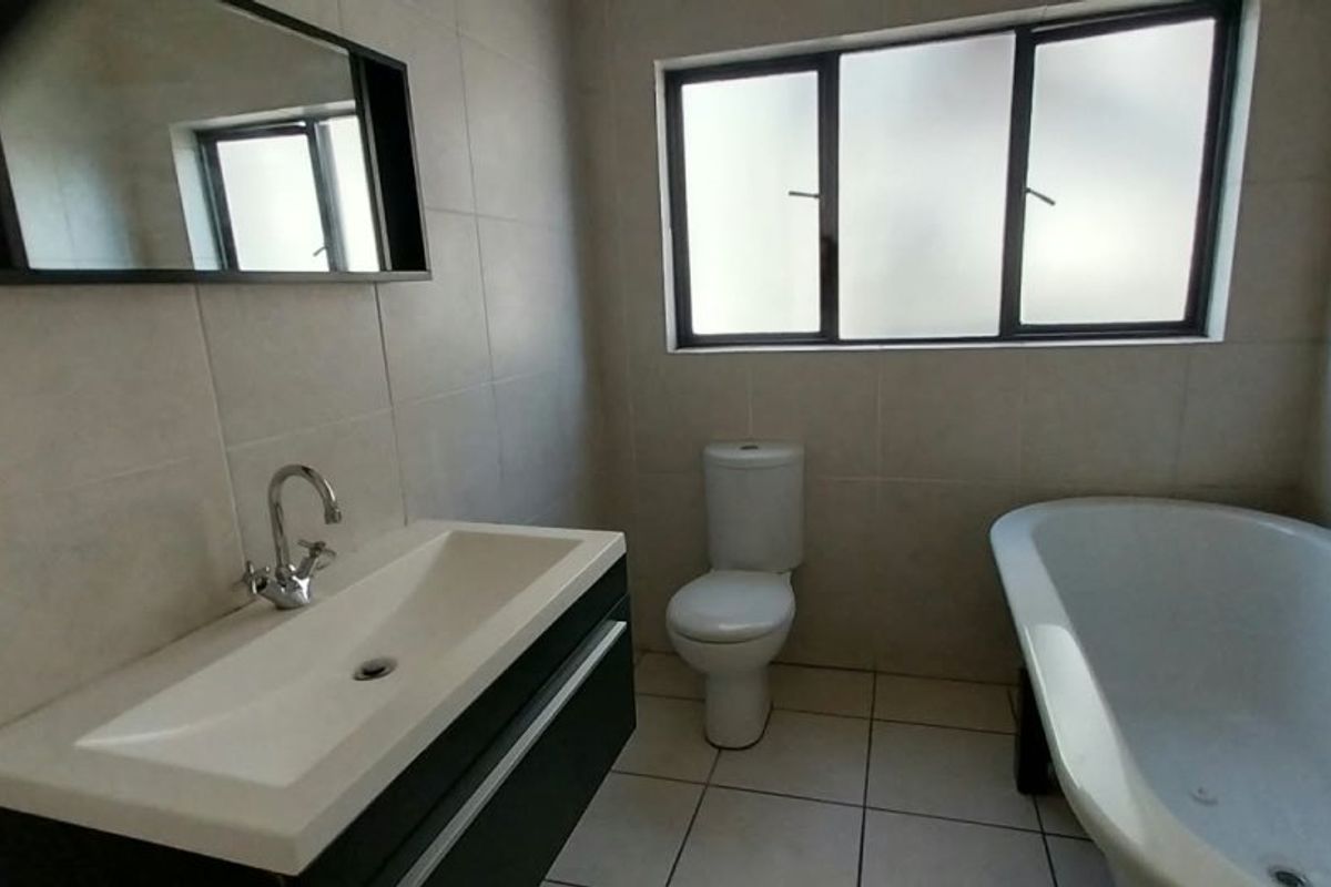 A clean, modern bathroom featuring a wall-mounted vanity, a freestanding bathtub, a toilet, and neutral ceramic tiling throughout.