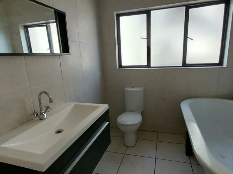 A clean, modern bathroom featuring a wall-mounted vanity, a freestanding bathtub, a toilet, and neutral ceramic tiling throughout.