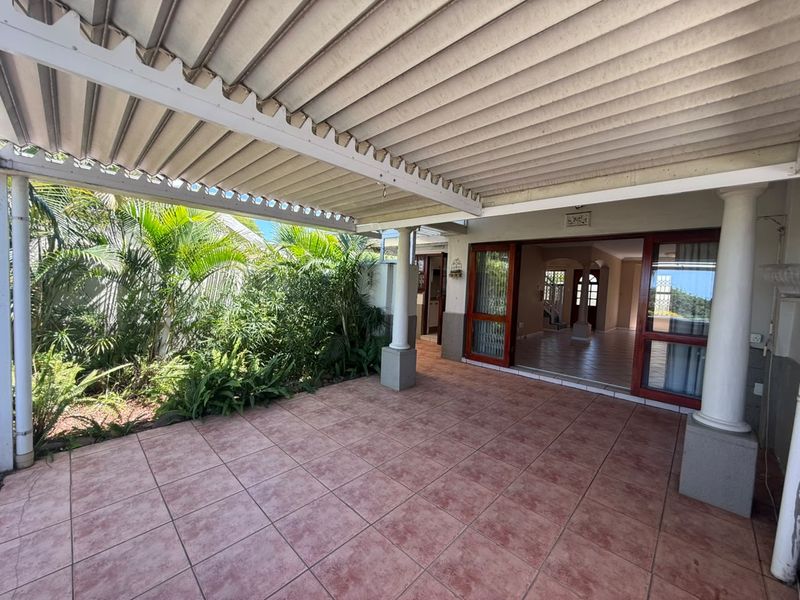 A covered outdoor patio area featuring tiled flooring and support columns, providing direct access to the interior living space through sliding glass doors.