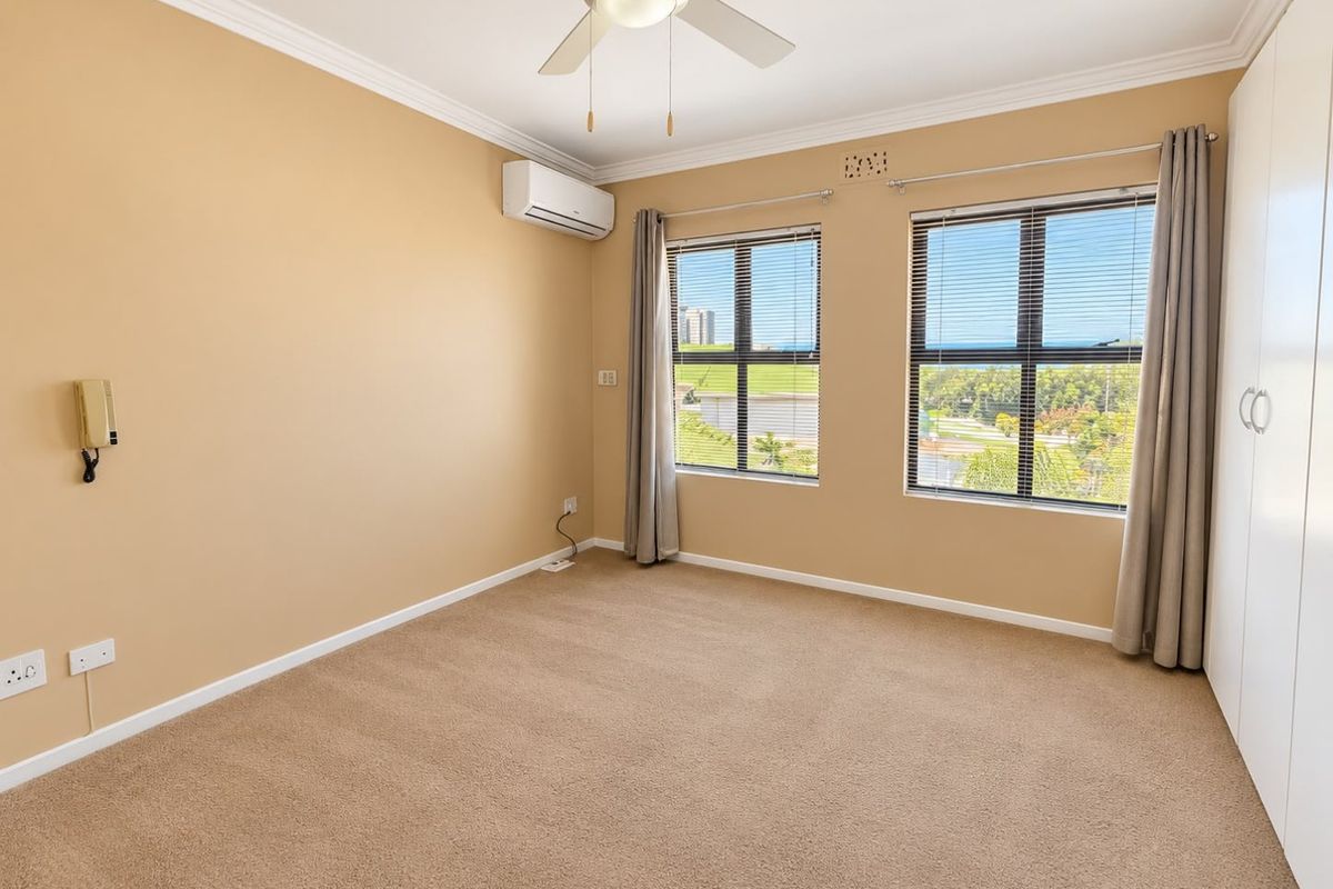 A spacious, empty bedroom featuring neutral carpeting, a ceiling fan, split-system air conditioning, and built-in wardrobes with pleasant exterior views.