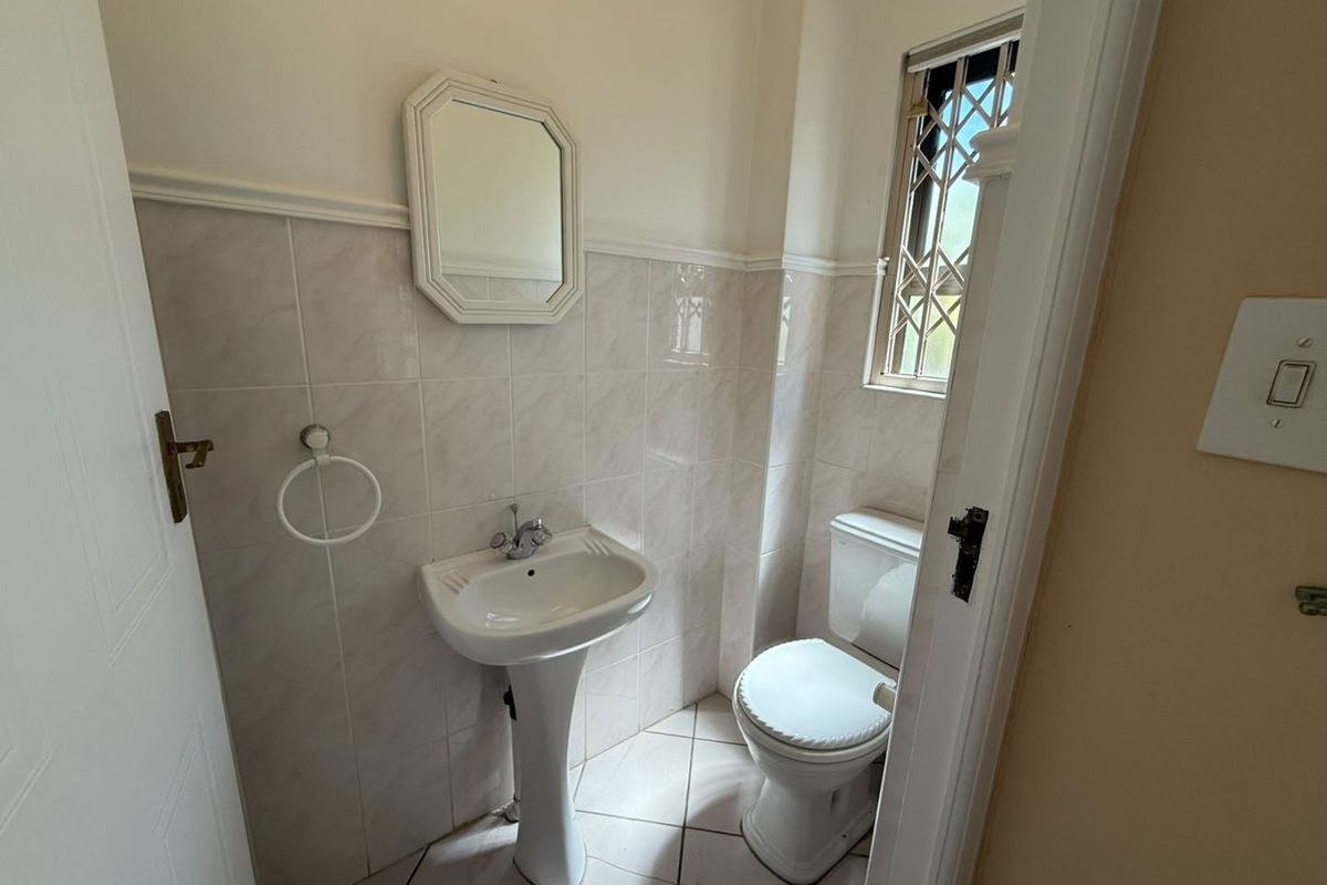 A compact guest bathroom featuring a pedestal basin, toilet, and neutral wall and floor tiling with a secure window.