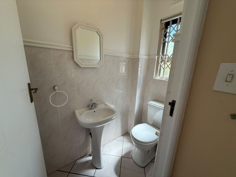 A compact guest bathroom featuring a pedestal basin, toilet, and neutral wall and floor tiling with a secure window.