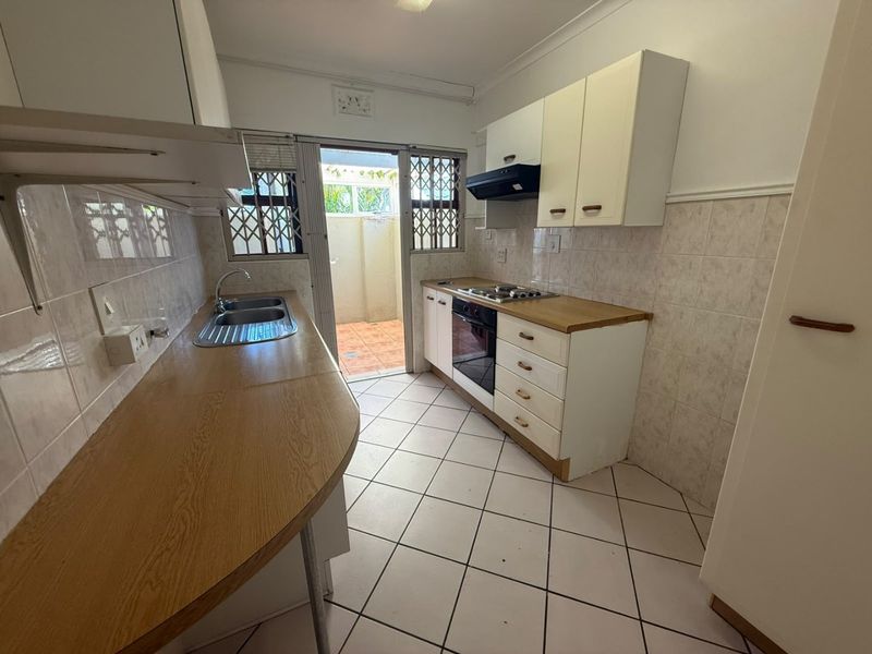 Functional kitchen featuring built-in cabinetry, laminate countertops, a gas hob, and direct access to an outdoor courtyard area.