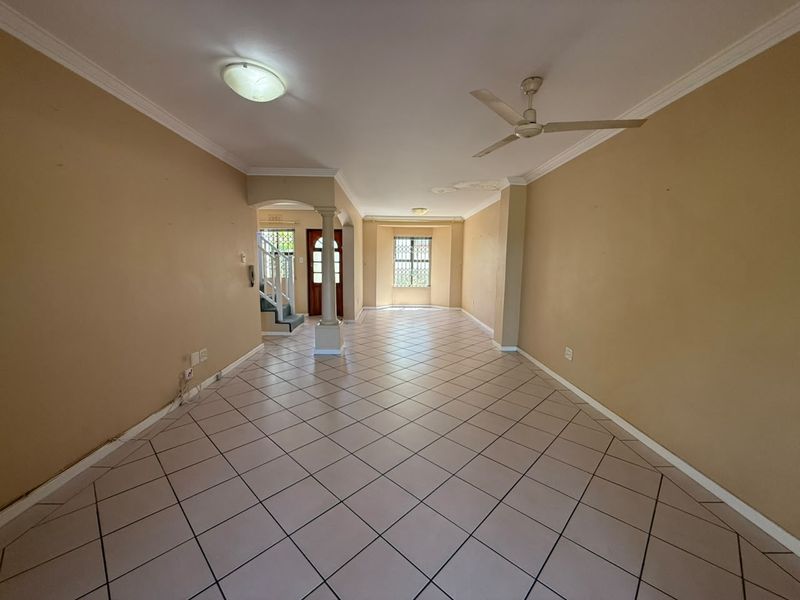 Spacious, empty living area featuring tiled flooring, a ceiling fan, and an archway leading to the entrance and staircase.