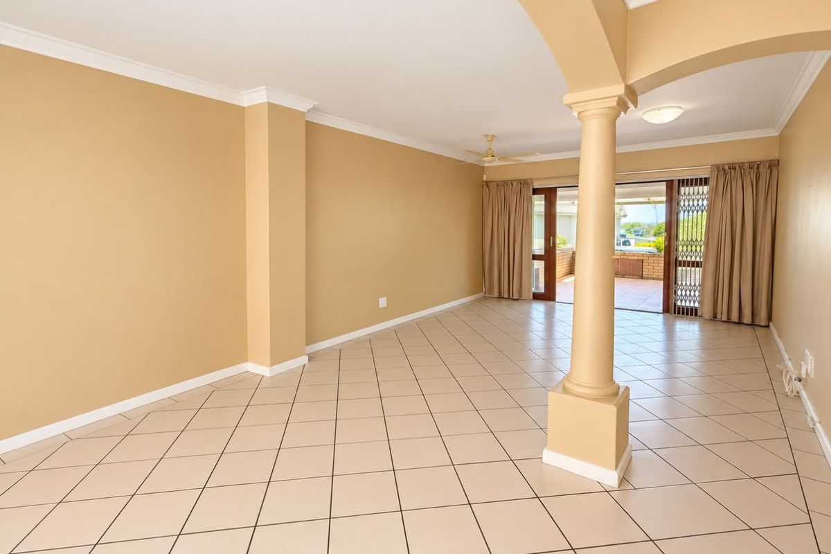 Spacious, open-plan living area featuring neutral ceramic tile flooring, a decorative column, and sliding glass doors leading to an outdoor patio.