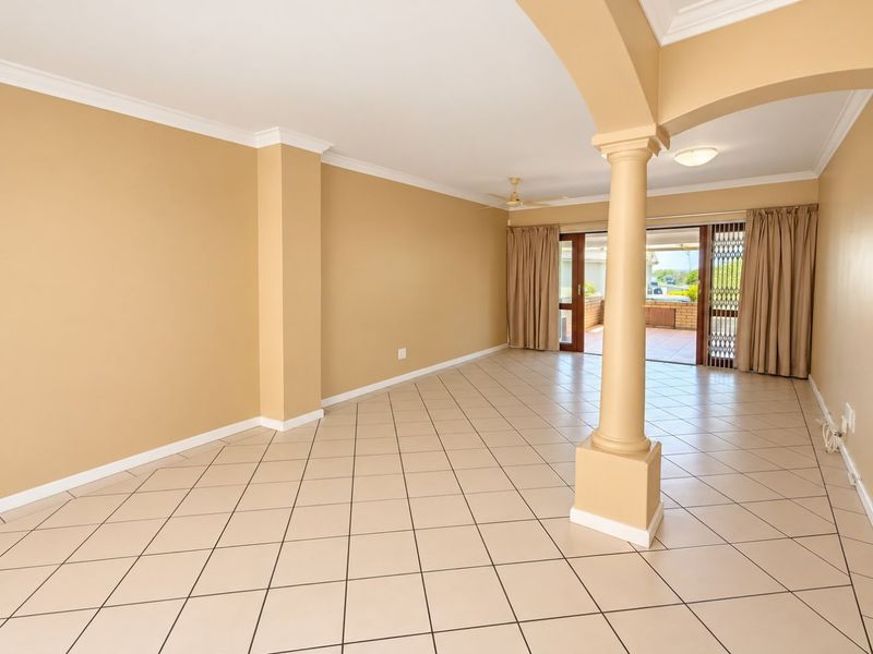 Spacious, open-plan living area featuring neutral ceramic tile flooring, a decorative column, and sliding glass doors leading to an outdoor patio.
