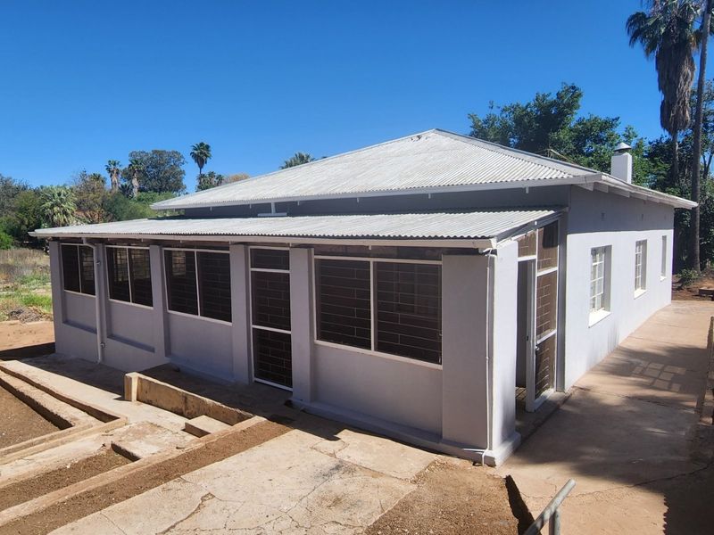 Rear view of the property featuring a corrugated metal roof, security-barred windows, and a concrete patio area with surrounding garden space.