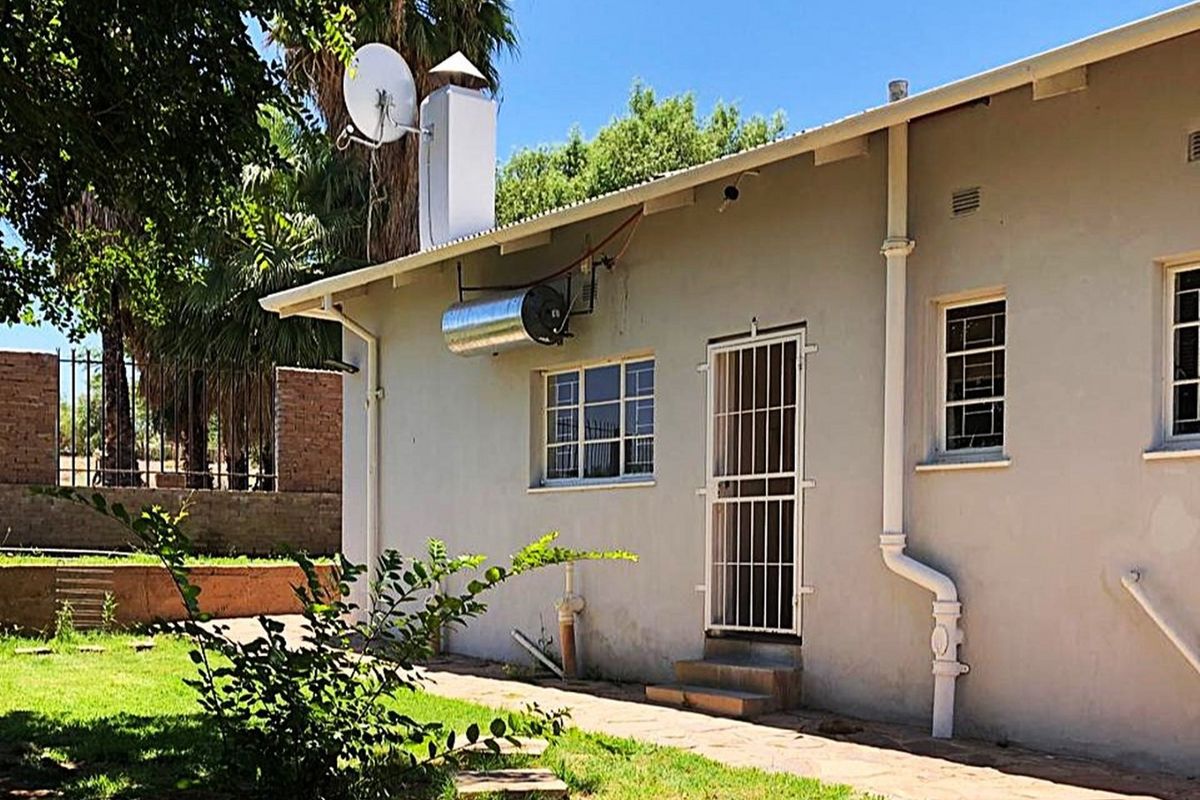 Rear exterior view of the house featuring a solar water heater, security gates, and a paved walkway leading along the building facade.