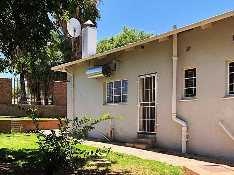 Rear exterior view of the house featuring a solar water heater, security gates, and a paved walkway leading along the building facade.