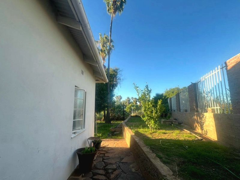 A side view of the property showing a stone paved walkway, retaining wall, and perimeter fencing along the garden area.