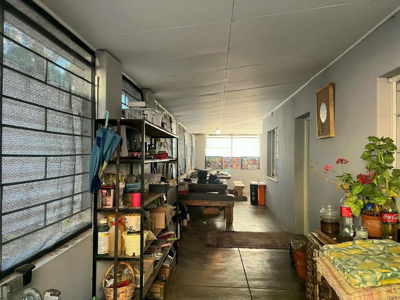 A covered patio or sunroom area featuring concrete flooring and large louvre windows with external security screens.