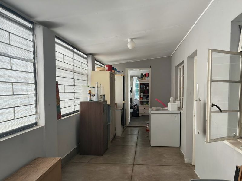 A functional utility space featuring tiled flooring and large windows with security bars, providing access to adjacent rooms.