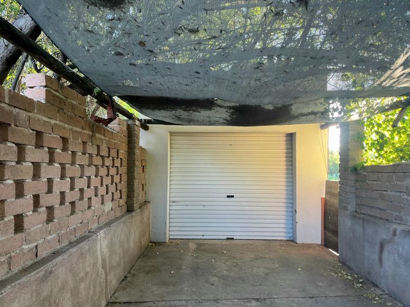 A functional garage space featuring a roller shutter door, concrete flooring, and a brick boundary wall with an overhead shade cloth canopy.