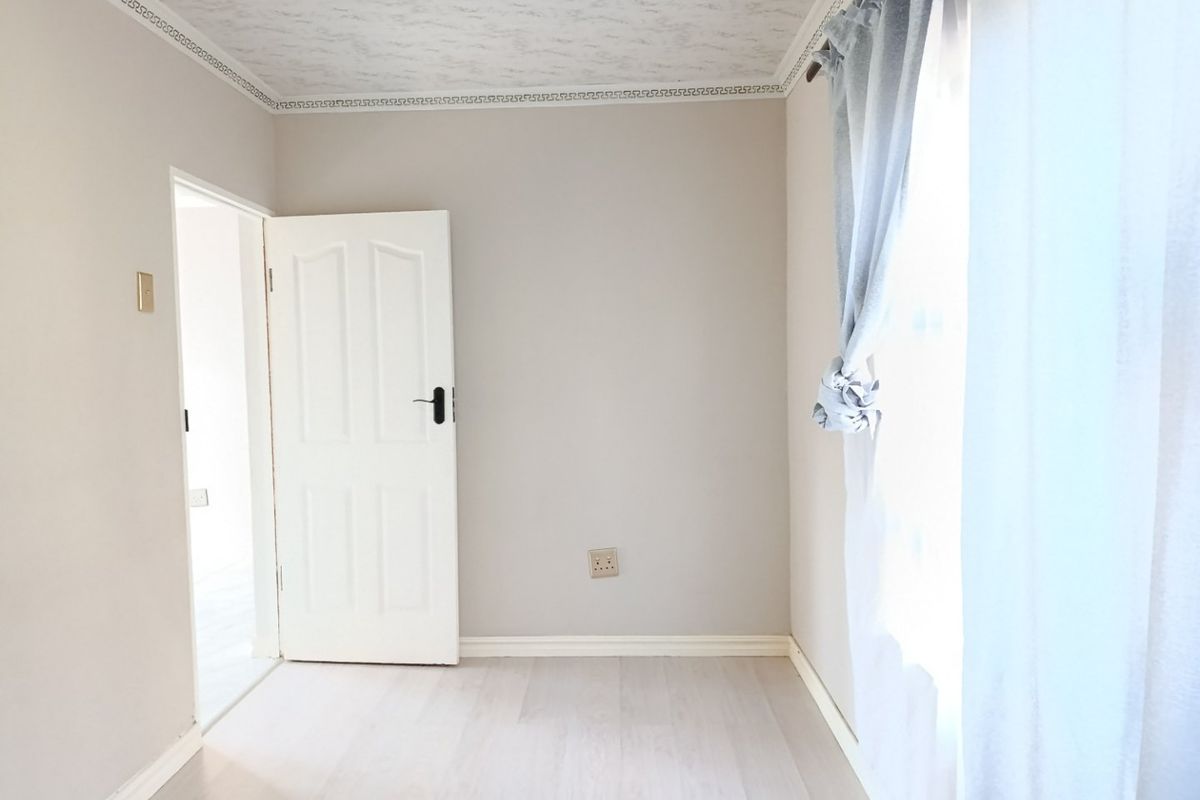 A bright, empty bedroom featuring light-toned laminate flooring, a textured ceiling with decorative cornice, and a neutral wall finish.