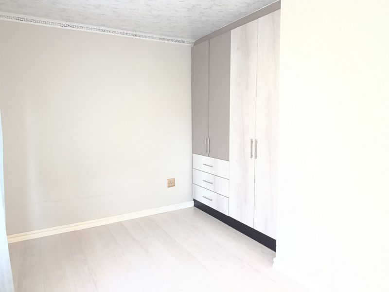 A bright, empty bedroom featuring modern built-in cupboards with a two-tone finish and light-toned laminate flooring.
