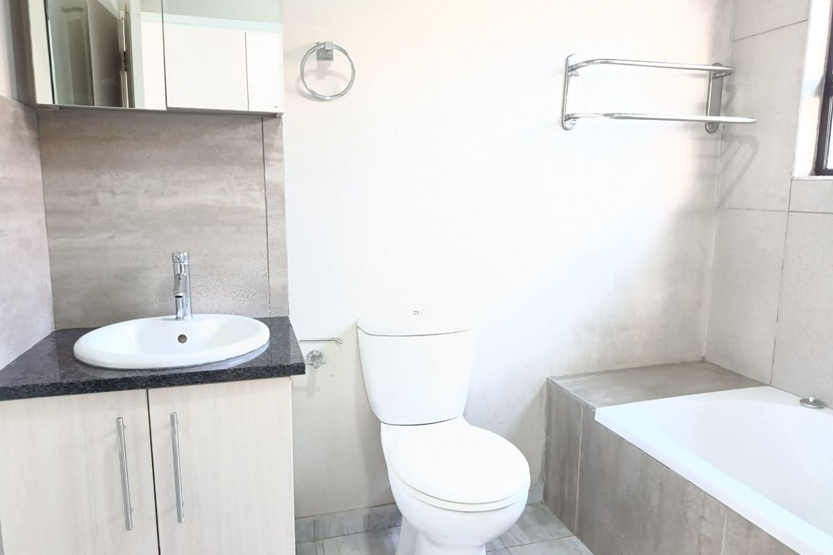 A clean and functional bathroom featuring a vanity with basin, a standard toilet, and a built-in bathtub with neutral wall and floor tiling.