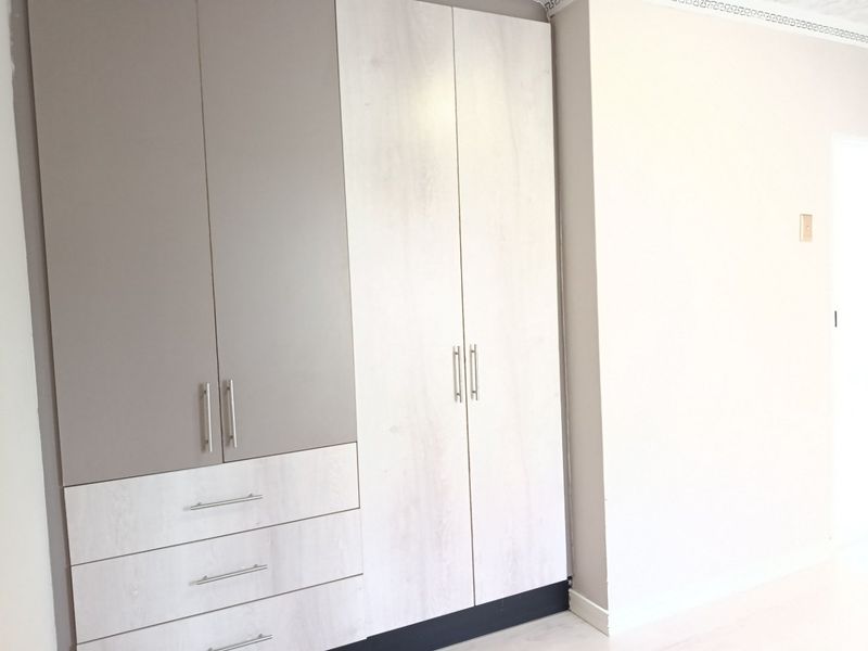 A clean, modern bedroom featuring neutral-toned built-in cupboards with integrated drawers and contemporary hardware.