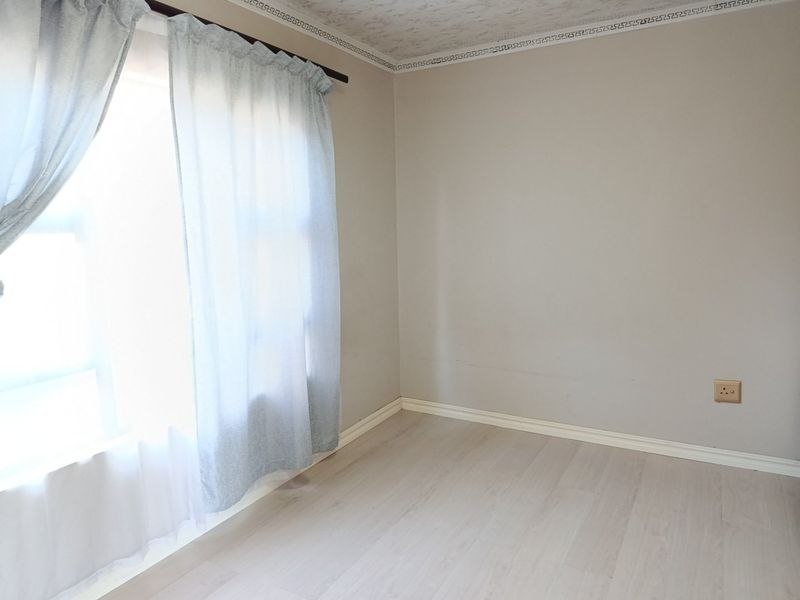 A bright, empty bedroom featuring light-toned laminate flooring, neutral wall paint, and decorative ceiling cornicing, offering a clean canvas for personalization.