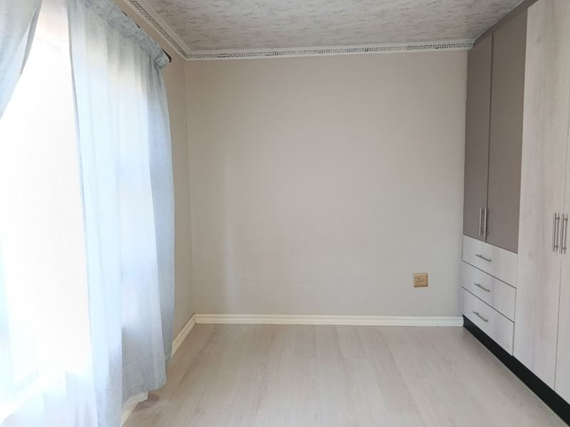 A bright, empty bedroom featuring modern laminate flooring, neutral walls, and ample built-in cupboard storage.