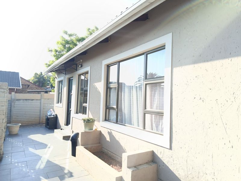 A view of the rear exterior featuring a tiled patio area, built-in planter box, and aluminium window frames along the building facade.