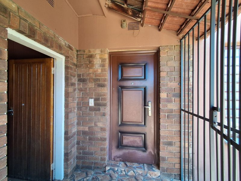 Entrance area featuring brick walls, a security gate, and tiled flooring, with visible wear to the roof eaves and door finish.