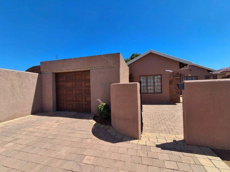 Front exterior view of the house featuring a paved driveway, single garage with timber door, and a secure boundary wall.