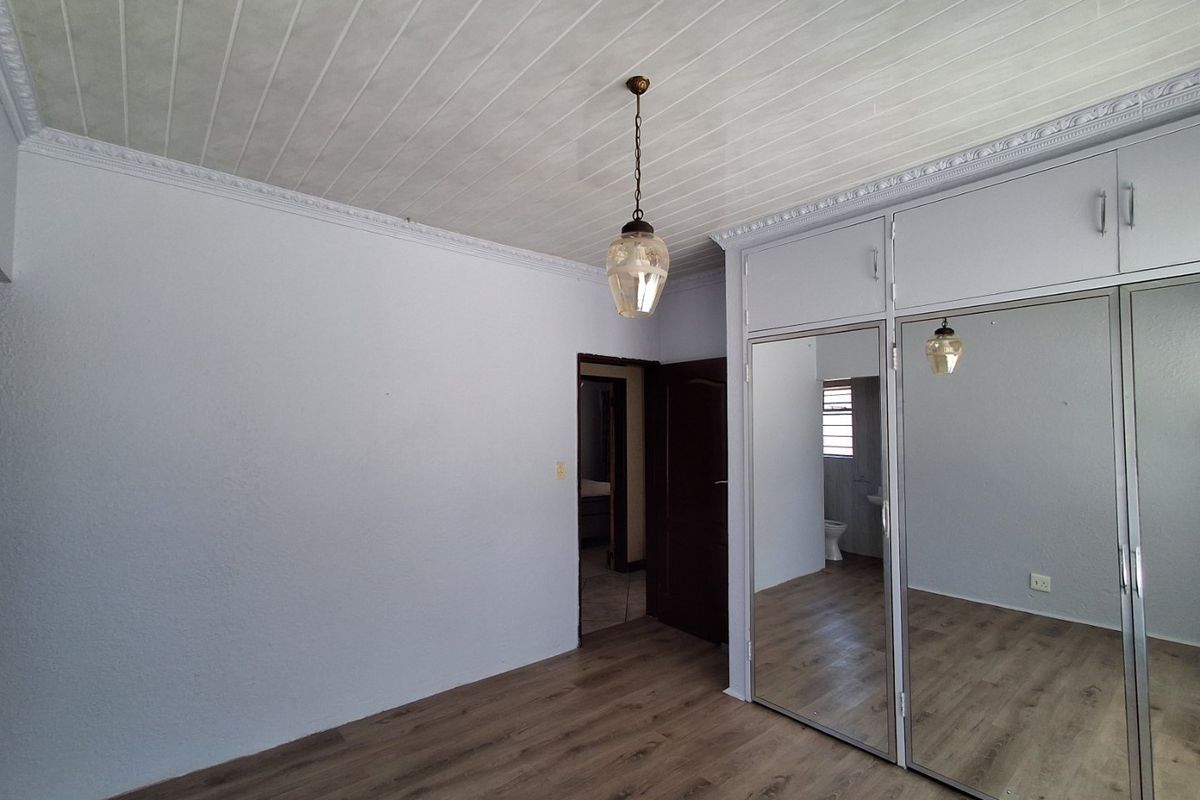 A bright, empty bedroom featuring modern laminate flooring, a panelled ceiling with decorative cornice, and large built-in cupboards with mirrored doors.
