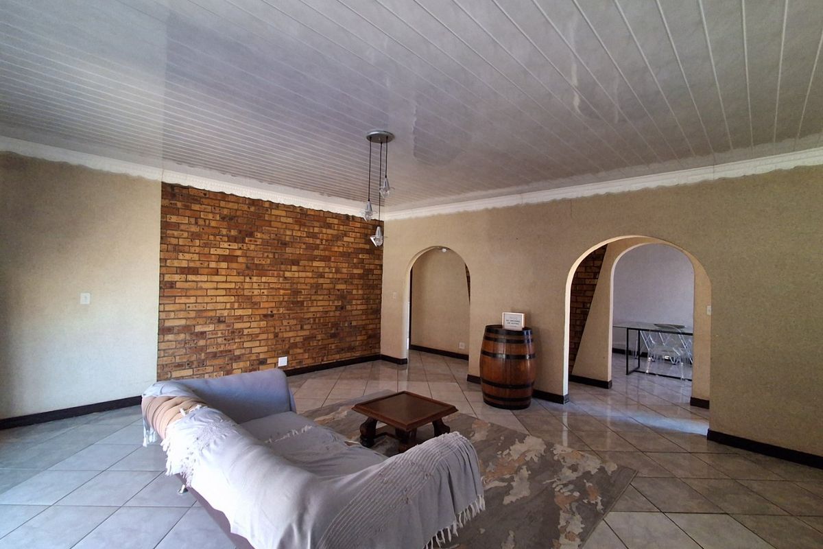 Spacious living area featuring an exposed brick feature wall, arched architectural details, tiled flooring, and a tongue and groove ceiling.
