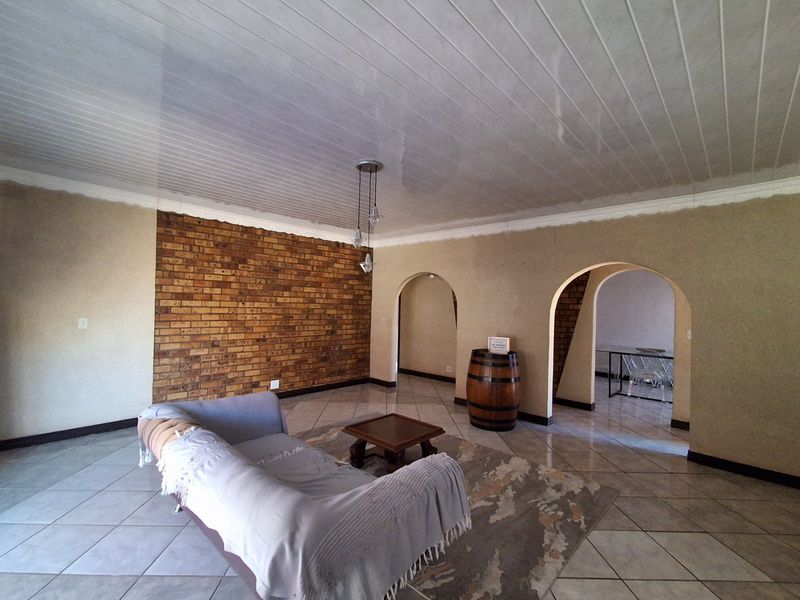 Spacious living area featuring an exposed brick feature wall, arched architectural details, tiled flooring, and a tongue and groove ceiling.