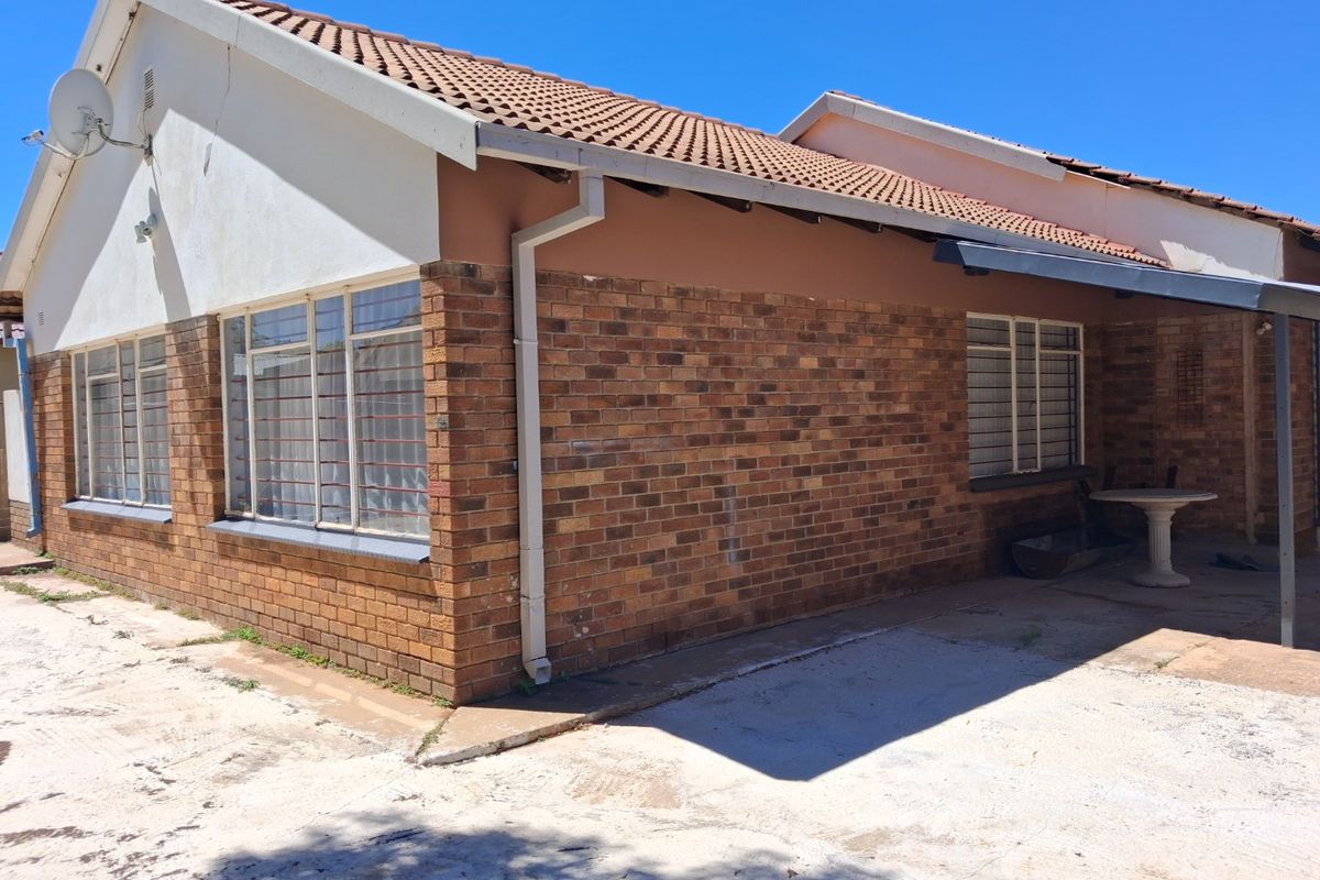 Rear exterior view of the house featuring face brick walls, a tiled roof, and a concrete patio area with security bars on the windows.