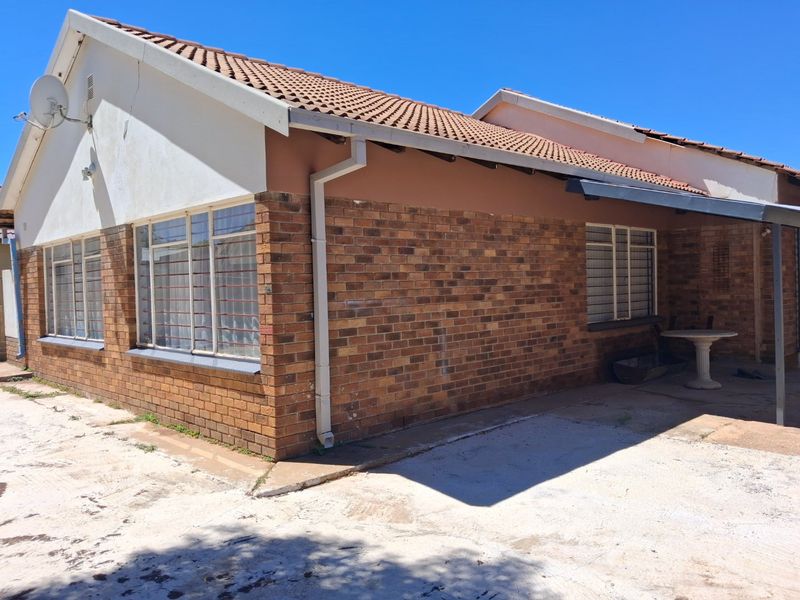 Rear exterior view of the house featuring face brick walls, a tiled roof, and a concrete patio area with security bars on the windows.