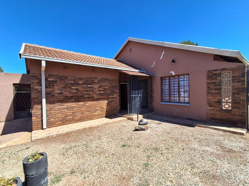 Front elevation of a single-story house featuring a combination of brick and plastered walls, a tiled roof, and security features.