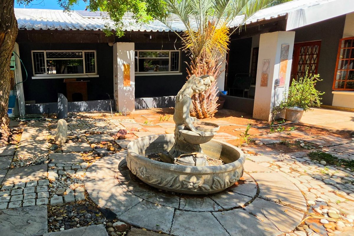 Rear courtyard area featuring a stone fountain, paved patio space, and a covered veranda with access to the main house.