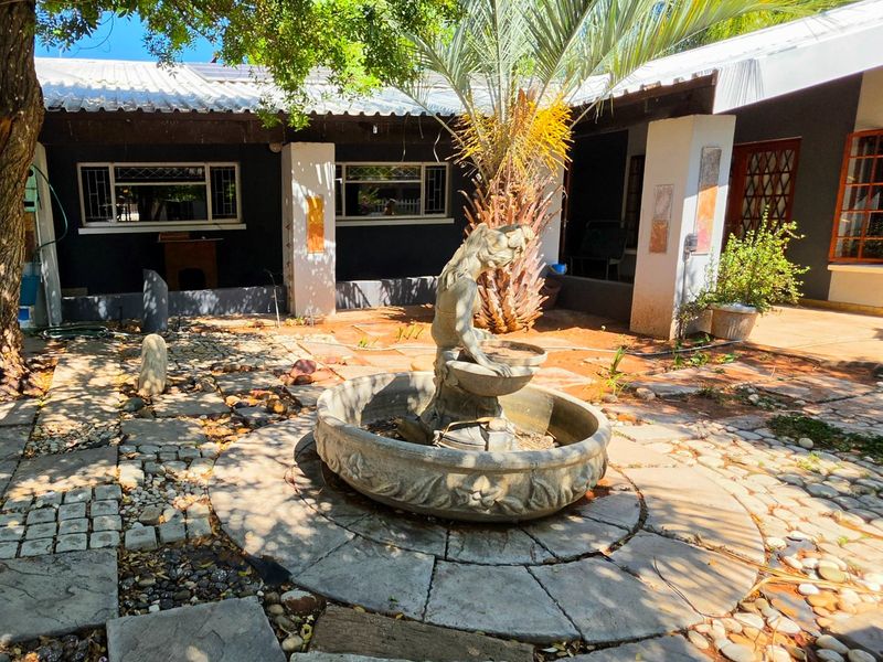 Rear courtyard area featuring a stone fountain, paved patio space, and a covered veranda with access to the main house.