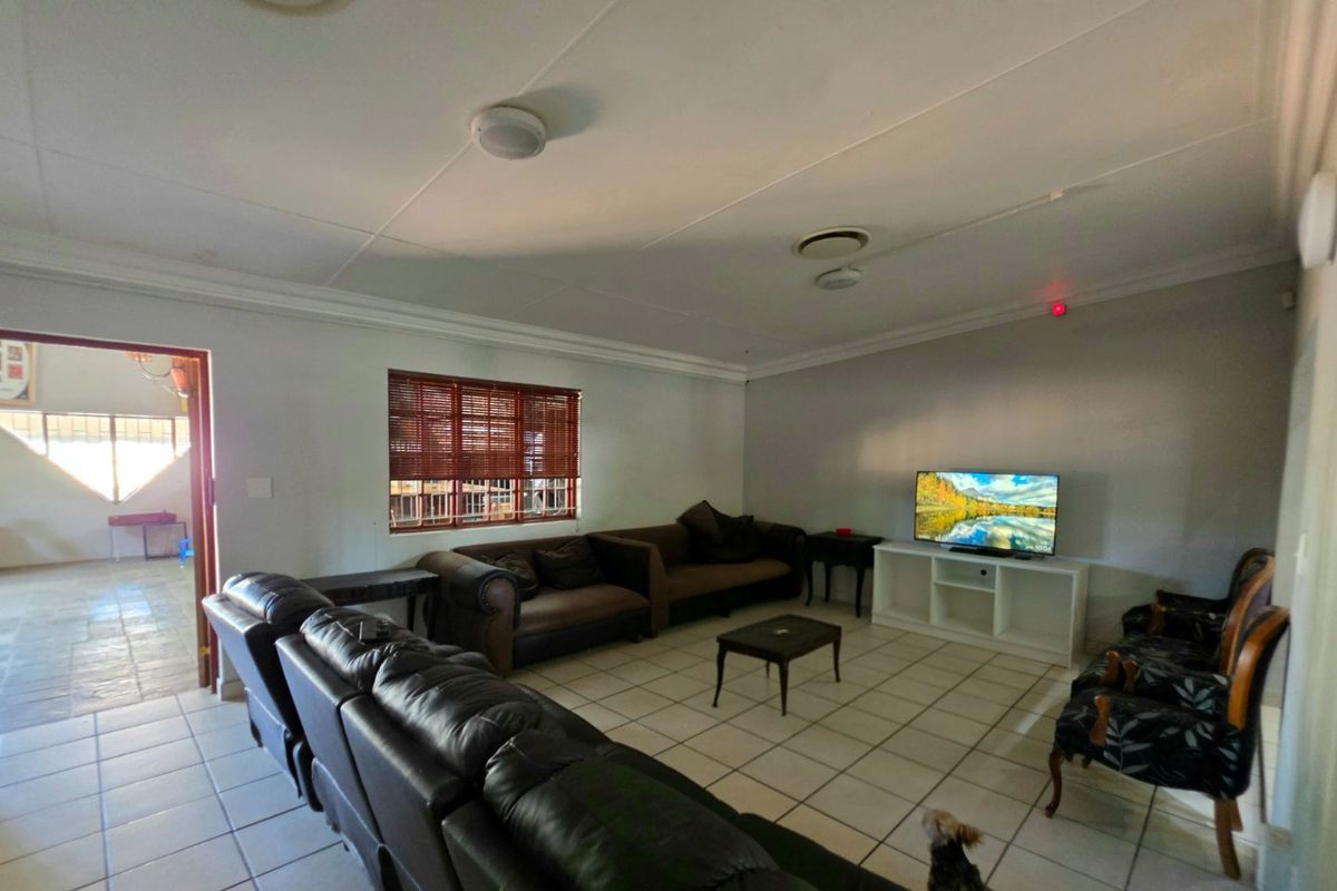 Spacious living room featuring tiled flooring, coved cornicing, and natural light through a window with fitted venetian blinds.