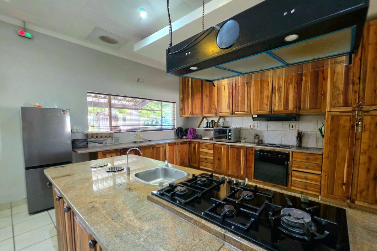 Spacious kitchen featuring extensive wooden cabinetry, granite countertops, a central island with a gas hob, and a built-in oven.