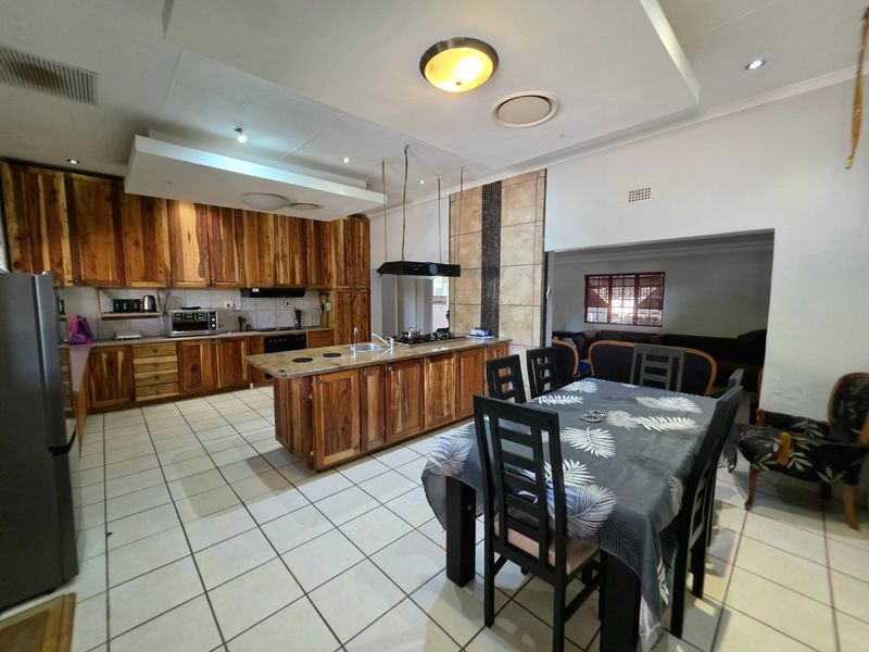 Spacious open-plan kitchen and dining area featuring extensive wooden cabinetry, a central island with a built-in hob, and tiled flooring throughout.