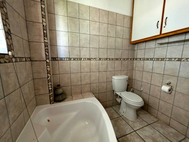 A functional bathroom featuring a built-in bathtub, toilet, and wall-mounted storage cabinetry with neutral tiled finishes throughout.