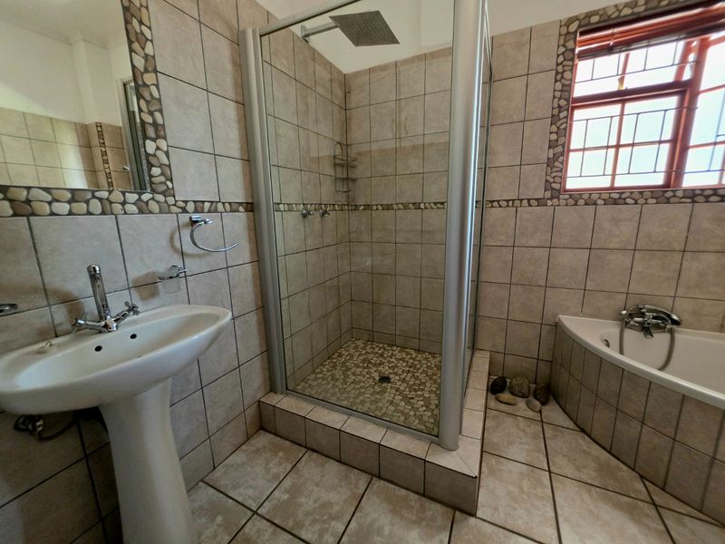 A functional bathroom featuring a pedestal basin, a corner bathtub, and a separate shower enclosure with tiled finishes throughout.
